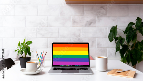 A modern home office setup with laptop and a rainbow flag on screen, for pride day. Generative AI. photo
