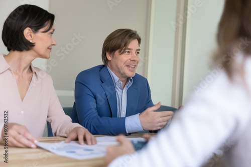 Mature boss makes speech during formal meeting with company clients, business trainer leads corporate training for staff members take part in group meeting in office. Negotiations, briefing, business