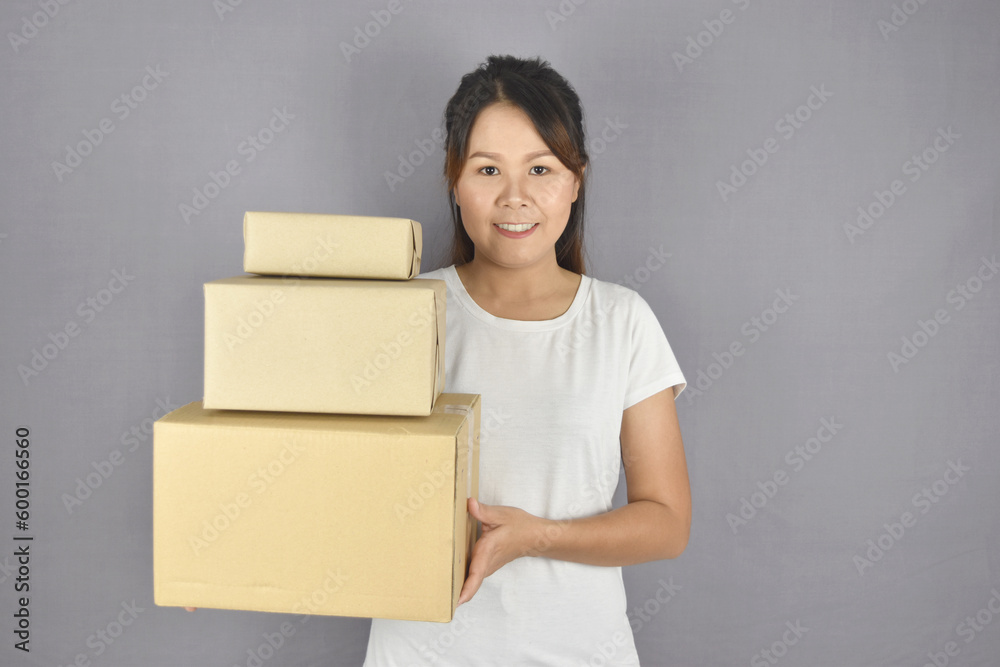 Asian woman smiling holding package box on grey background. Delivery and customer services concept. Asian woman smiling holding package box on grey background. Delivery and customer services concept.