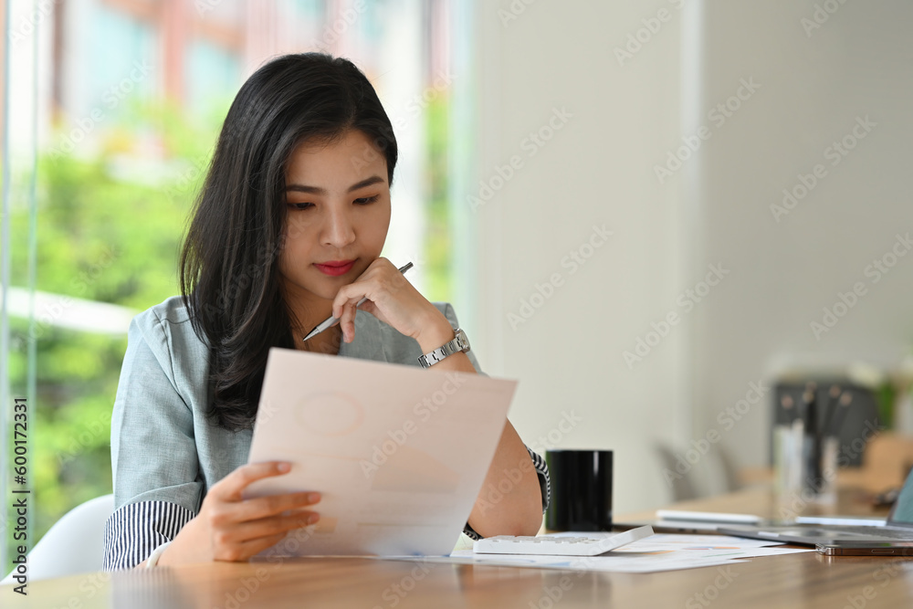 Portrait of serious asian businesswoman analyzing business information documents at her office desk. Portrait of serious asian businesswoman analyzing business information documents at her office desk.