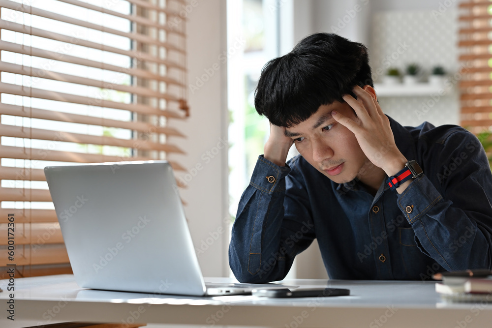 Tired exhausted Young Asian man, office worker, businessman or freelancer, sitting at his desk, tired of working in a laptop, overworked, having a headache. Tired exhausted Young Asian man, office worker, businessman or freelancer, sitting at his desk, tired of working in a laptop, overworked, having a headache.