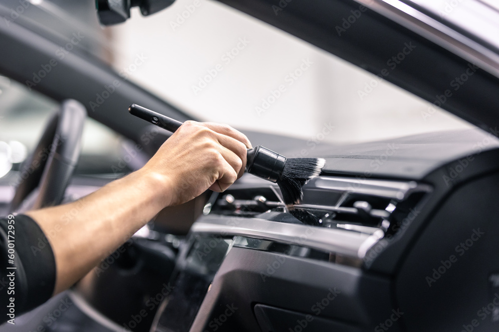 Professional detailing a car in the studio, hands with brush cleaning car interior from a dust, vehicle care concept