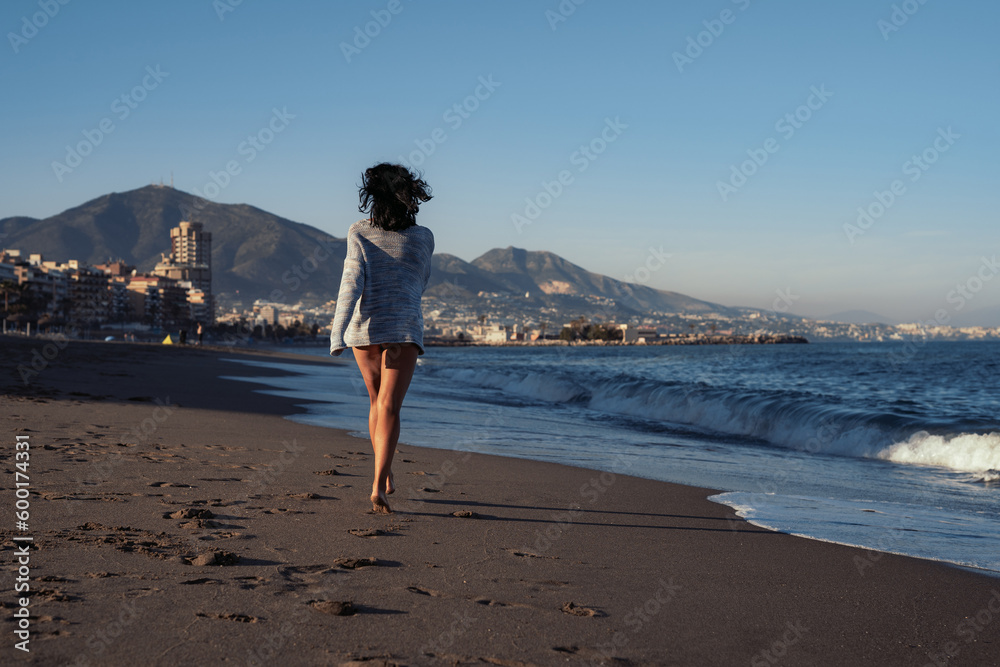 young beautiful brunette girl walks on the sand on the seashore in a swimsuit and a sweater