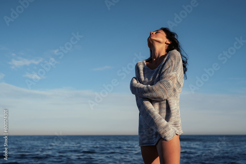 young beautiful brunette girl walks on the sand on the seashore in a swimsuit and a sweater