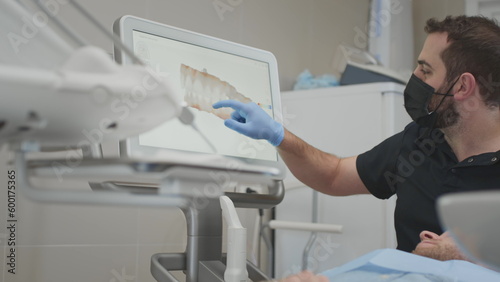 A male orthodontist doctor shows on the display a 3d model of the oral cavity of a man patient. Medical examination of teeth. Digital scanning with a scanner, checking the jaw