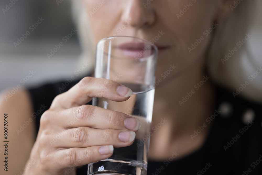 Transparent glass of pure fresh clean mineral water in mature female hand. Cropped shot of woman drinking water, keeping healthy hydration balance, detox diet. Close up focus on object