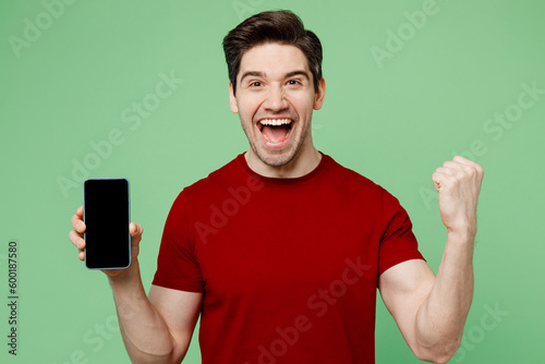 Young man he wearing red t-shirt casual clothes hold in hand use mobile cell phone with blank screen workspace area do winner gesture isolated on plain pastel light green background studio portrait.