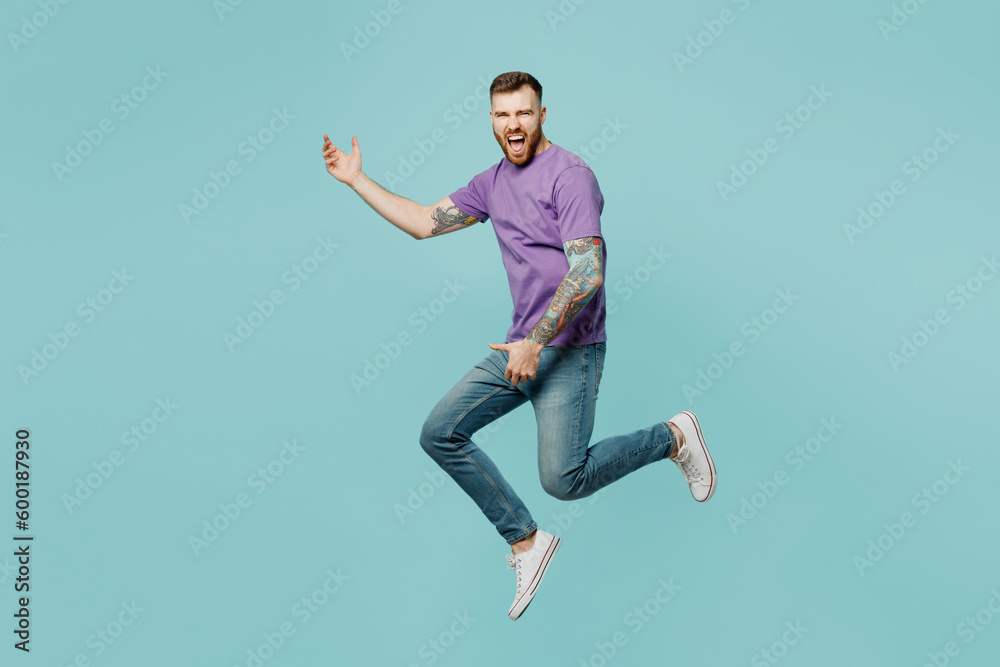 Full body singer excited happy young man he wears purple t-shirt jump high pov playing guitar, do hand gesture isolated on plain pastel light blue cyan background studio portrait. Lifestyle concept. - obrazy, fototapety, plakaty 