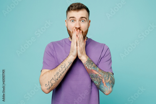 Young shocked surprised amazed fun man he wears purple t-shirt look camera cover mouth with hands isolated on plain pastel light blue cyan background studio portrait. Tattoo translates life is fight. photo