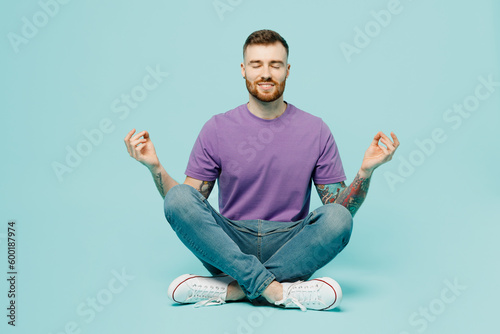 Fototapeta Naklejka Na Ścianę i Meble -  Full body young man wear purple t-shirt hold spreading hands in yoga om aum gesture relax meditate try to calm down isolated on plain pastel light blue cyan background Tattoo translates life is fight