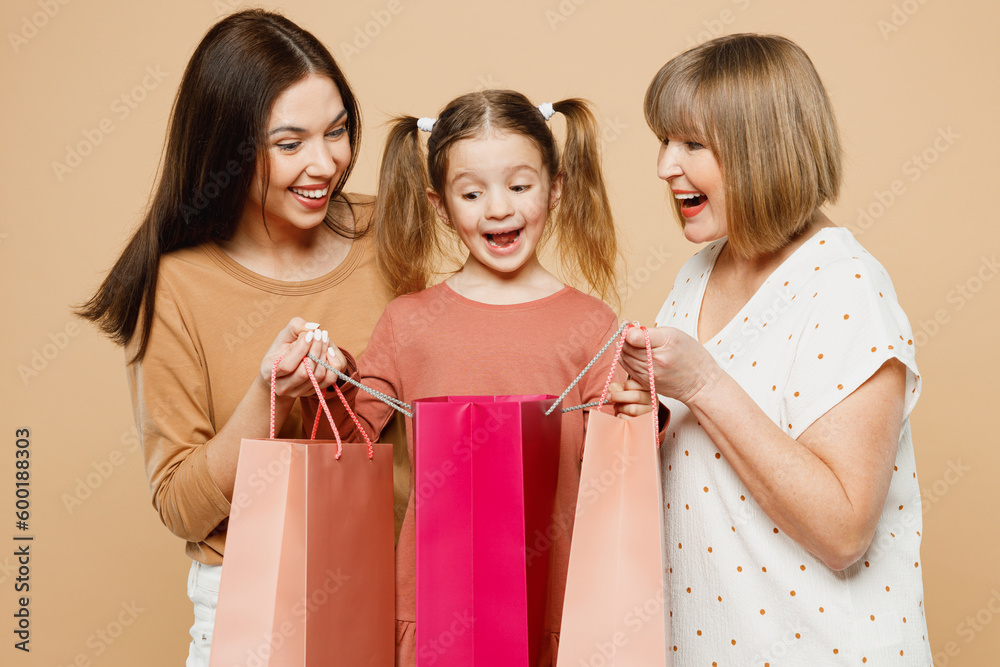 Happy women wearing casual clothes with child kid girl 6-7 years old. Granny mother daughter hold open shopping package isolated on plain beige background. Family parent day Black Friday sale concept. Happy women wearing casual clothes with child kid girl 6-7 years old. Granny mother daughter hold open shopping package isolated on plain beige background. Family parent day Black Friday sale concept.