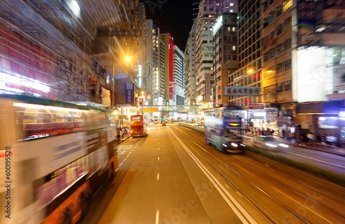 Night scape of trolley cars and double-decker buses dashing on a busy street flanked by office towers and colorful neon signs, in vibrant Mong Kok commercial district, in Kowloon Downtown, Hong Kong