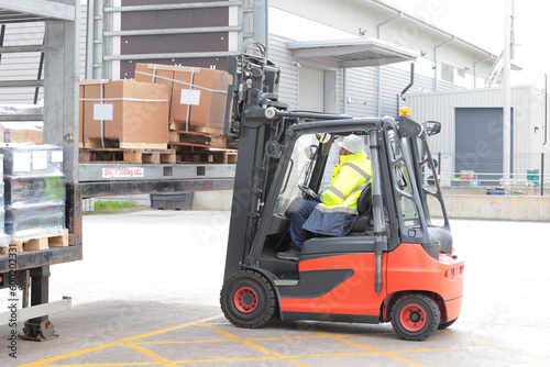 Forklift driver loading pallet on lorry trailer for transport to customer