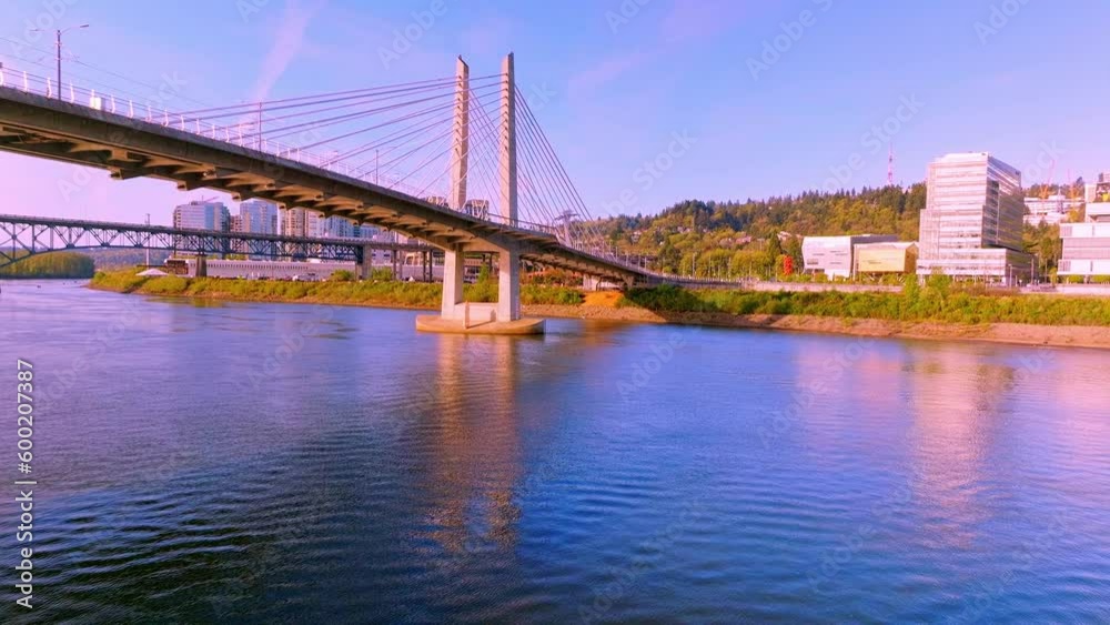 A beautiful aerial flying backwards of Tilikum Crossing Bridge's twin towers, cables, and stunning architecture with fishing boats in Portland, just above the water.