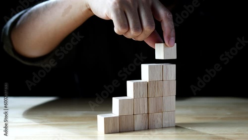 Business development to success. Businessman hand stacking wood block as step stair, business growth success on dark background. Concept of Business growth, Financial planning, Investment, Strategy