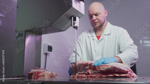 Industrial processing of meat. A man cook cuts a piece of tenderloin in a butcher's shop on a machine with a band saw. Ribeye or marbled beef. photo