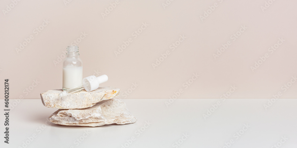 Φωτογραφία Glass dropper bottle with white serum or cream on stand from natural stone, beige pastel background, banner with copy space