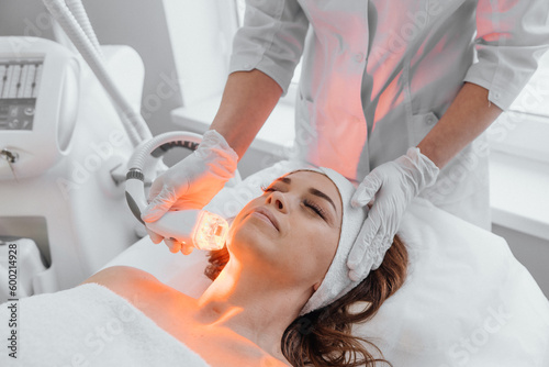 The hardware anti-aging procedure is an innovative method that helps restore skin health, get rid of wrinkles and increase its elasticity. Beautician uses LED therapy in beauty salon photo