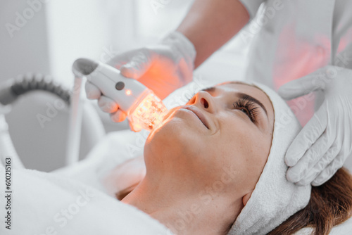 Photo using LED therapy, taken in a dermatological clinic. Light therapy accelerates healing and improves skin condition by reducing lines and wrinkles. Girl at the cosmetologist on the procedure photo