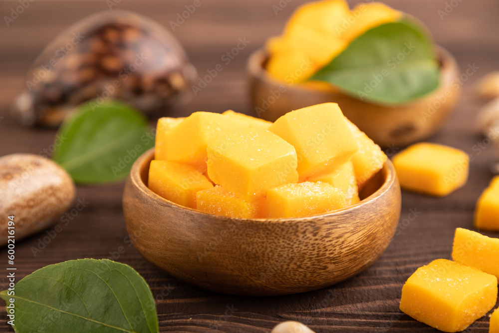 Dried mango cubes in wooden bowls on brown wooden, side view, selective focus. Dried mango cubes in wooden bowls on brown wooden, side view, selective focus.