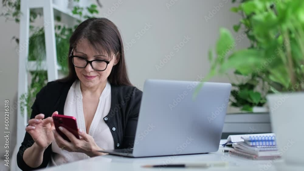 Middle aged woman in workplace home office using smart phone Middle aged woman in workplace home office using smart phone