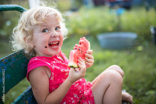 little girl eats watermelon in the summer sitting in the country on an old bench. Happy childhood.