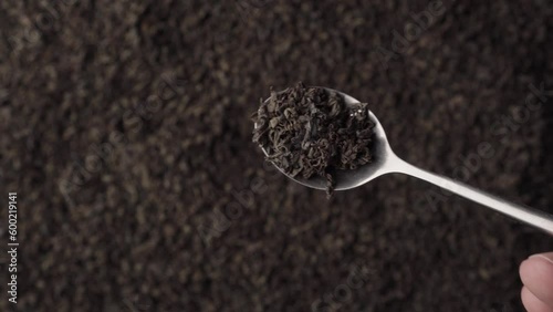 A teaspoon scooping up black fanning or broken loose leaf tea and being examined in detail. Close up, top view photo