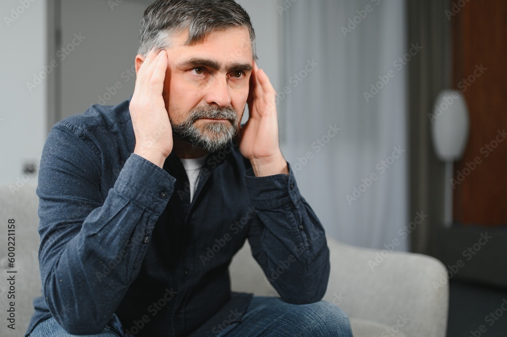Closeup of middle-aged bearded man suffering from headache at home, touching his temples, panorama with copy space. Migraine, headache, stress, tension problem, hangover concept Closeup of middle-aged bearded man suffering from headache at home, touching his temples, panorama with copy space. Migraine, headache, stress, tension problem, hangover concept