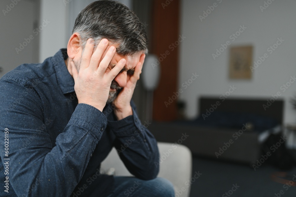 Middle age grey-haired man stressed sitting on sofa at home Middle age grey-haired man stressed sitting on sofa at home