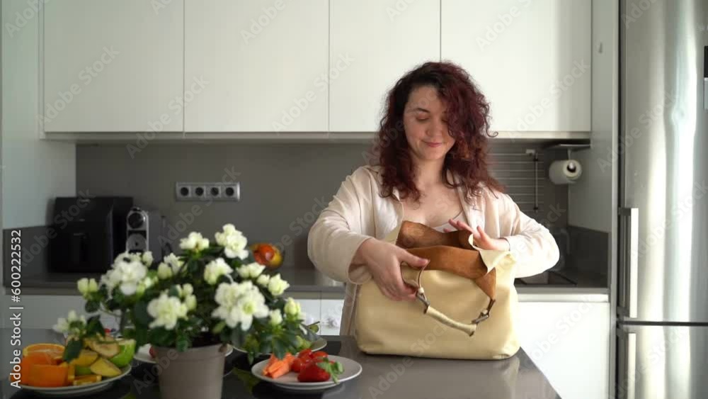 lunch box in beige big bag. Beautiful young woman getting ready to go to work. Sunny modern kitchen with fruits and flowers. Every day healthy habits style video footage lunch box in beige big bag. Beautiful young woman getting ready to go to work. Sunny modern kitchen with fruits and flowers. Every day healthy habits style video footage