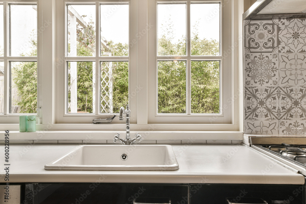 a kitchen sink in front of two windows with flowers on the wall behind it and a window to the outside a kitchen sink in front of two windows with flowers on the wall behind it and a window to the outside