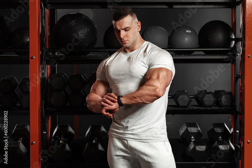 Muscular man looking at his watch in gym, schedule. Athletic male wears sportswear