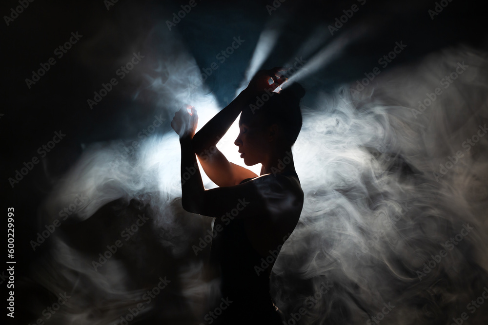 Dancer in a modern style poses against the background of smoke and flood lights. - obrazy, fototapety, plakaty 