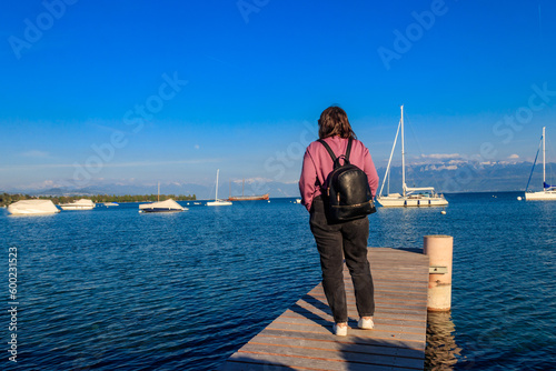 Back view of girl with backpack stand on wooden pier and looking the Alps and Lake Geneva in Switzerland