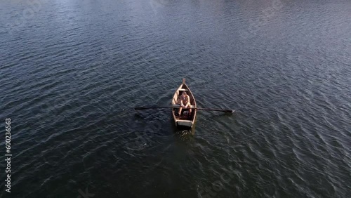 A lonely man oaring the boat at middle of lake.