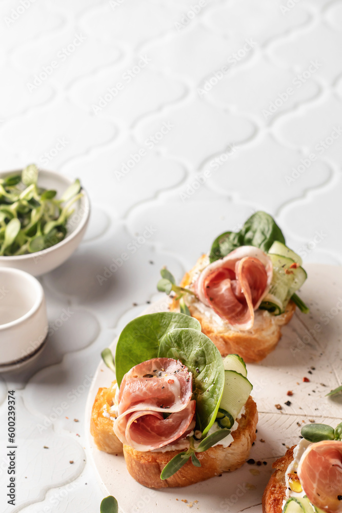 Bruschetta with ham or prosciutto, cream cheese, cucumber, spinach and microgreens. Tasty sandwich or toasted bread on white tile background. Tasty appetizer or breakfast, text space