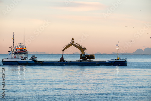 Fishing boat with Gibraltar in the background at sunrise and birds around it.