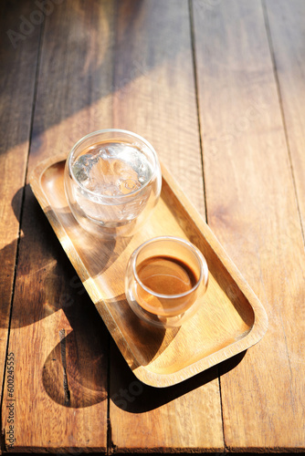 Hot coffee and glass of ice on wooden tray under sunlight