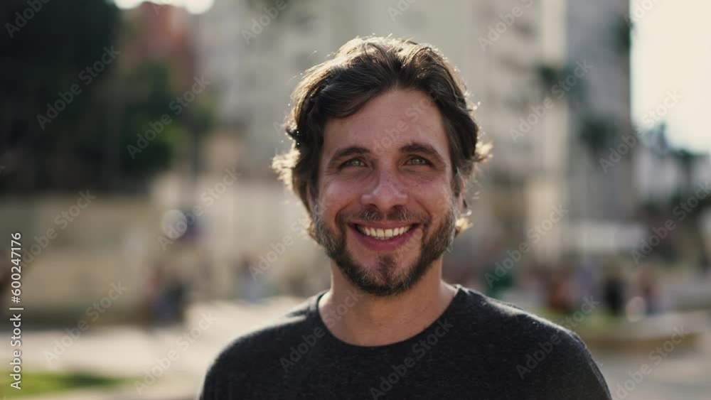 Portrait of a happy young handsome man smiling at camera standing outdoors at city park. A millennial caucasian male person in 30s looking at camera