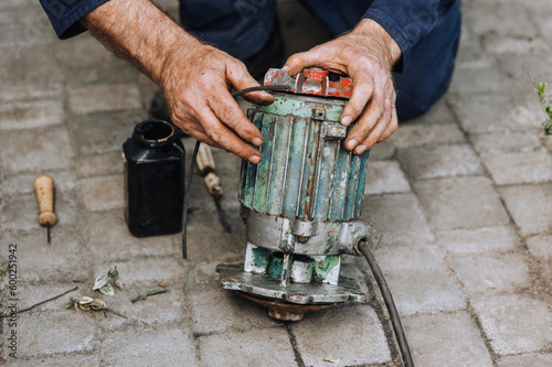 Male professional, electrician, electromechanic repairing an old rusty electric motor in a workshop. Photography, close-up portrait.