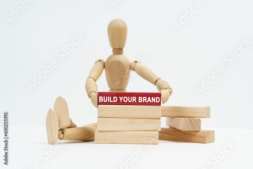 On a white surface sits a wooden man in his hands a block with the inscription - Build Your Brand