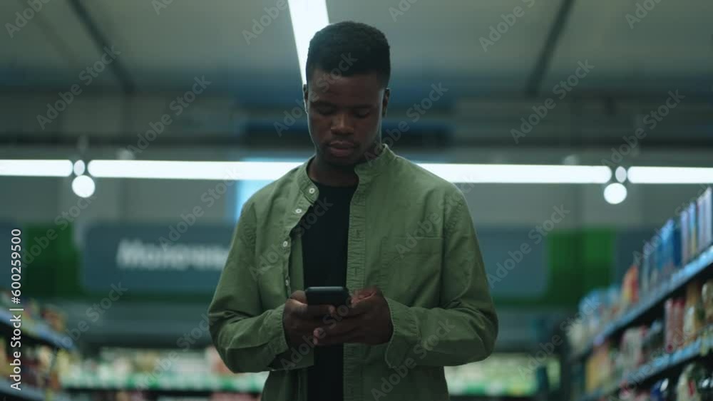 Black man browsing fresh produce in a grocery store, using a smartphone to find the best deals on healthy food Black man browsing fresh produce in a grocery store, using a smartphone to find the best deals on healthy food