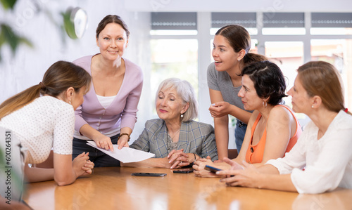 Smiling interested woman conducting informal work meeting with mixed age group of female colleagues sitting around table in office  discussing new strategies  projects  or work-related problems