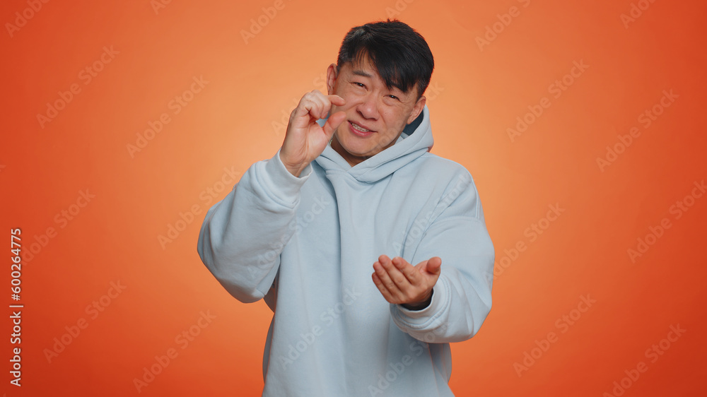 Need some more, please give me. Asian man showing a little bit gesture with sceptic smile, showing minimum sign, measuring small size. Handsome chinese guy isolated alone on orange studio background Need some more, please give me. Asian man showing a little bit gesture with sceptic smile, showing minimum sign, measuring small size. Handsome chinese guy isolated alone on orange studio background