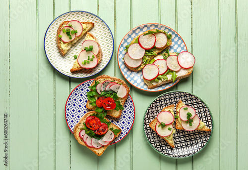 Plates with delicious radish bruschettas on green wooden table
