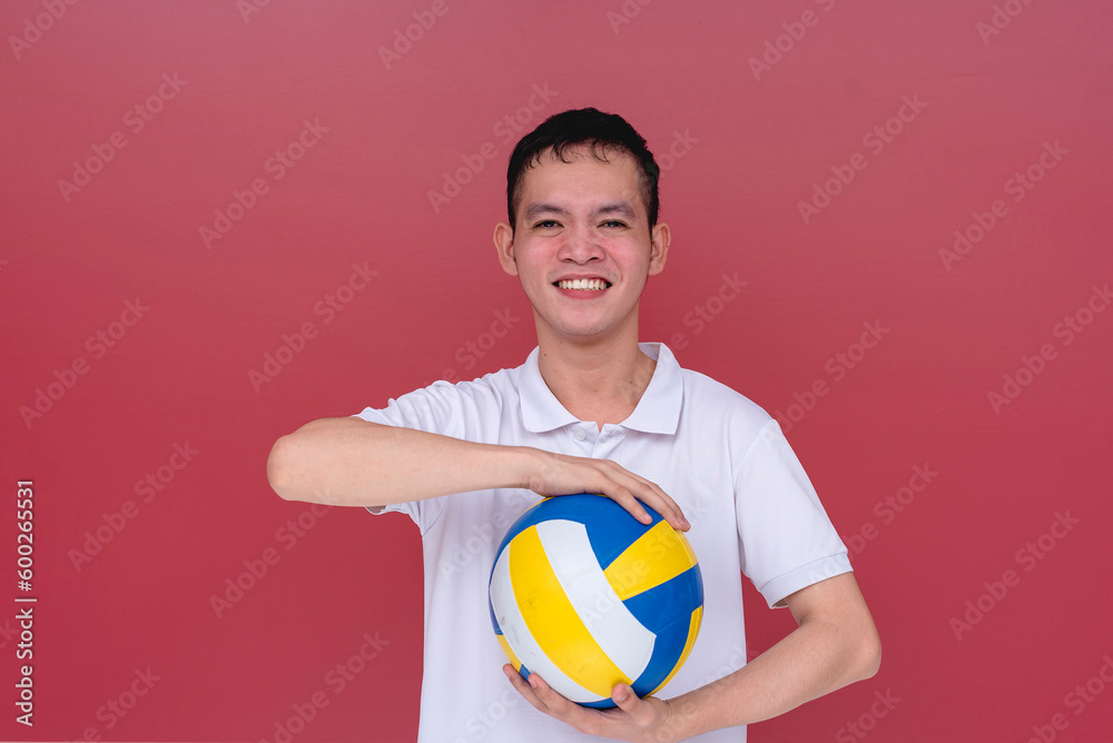 A sporty and athletic young man holding a volley ball between his hands. Isolated on a red background.