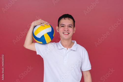 A sporty and athletic young man holding a volley ball between a hand and a shoulder. Isolated on a red background.