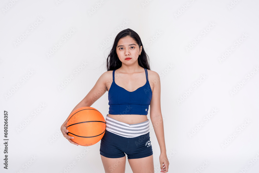 A sporty and athletic young woman posing while holding basketball on the side with both hands. Isolated on a white background. A sporty and athletic young woman posing while holding basketball on the side with both hands. Isolated on a white background.
