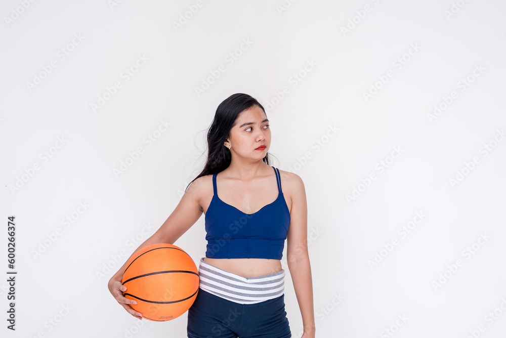 A sporty and athletic young woman posing while holding basketball on the side with one hand. Isolated on a white background.