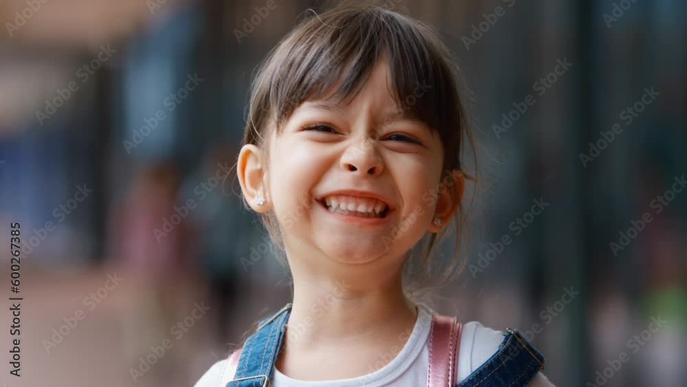 Head and shoulders portrait of smiling female elementary school student wearing backpack standing outside school building - shot in slow motion Head and shoulders portrait of smiling female elementary school student wearing backpack standing outside school building - shot in slow motion